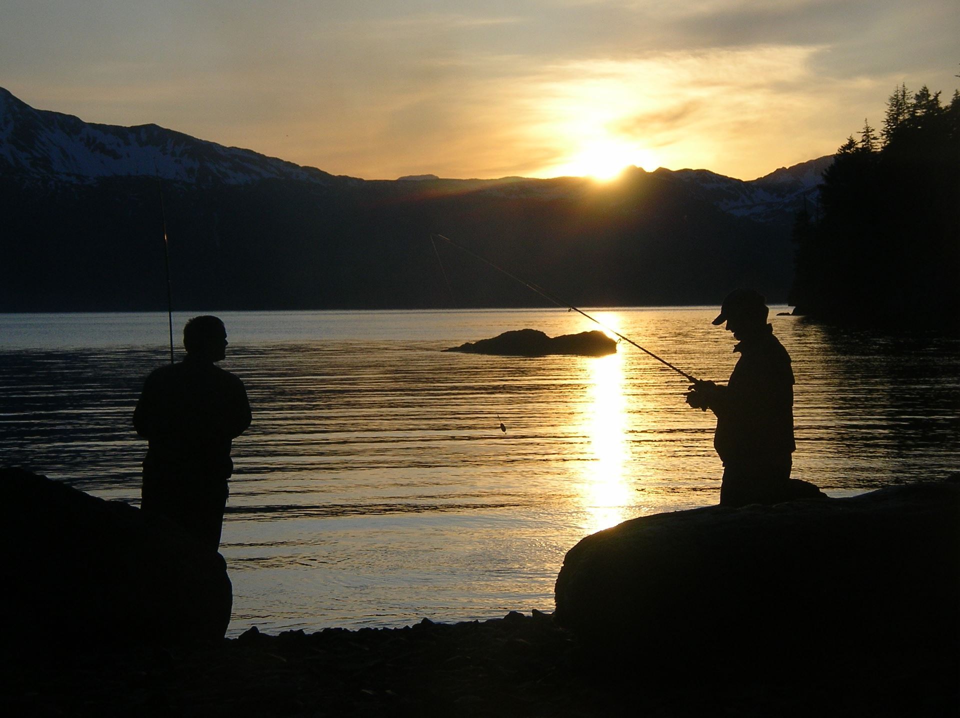 Two people fishing in a cove during sunset Photo